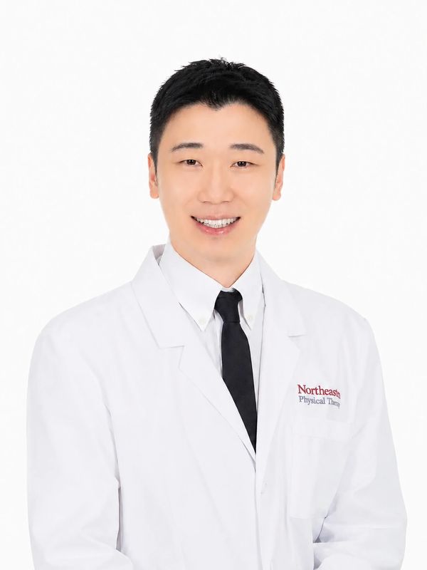 A smiling man in a white lab coat with a black tie against a white background.