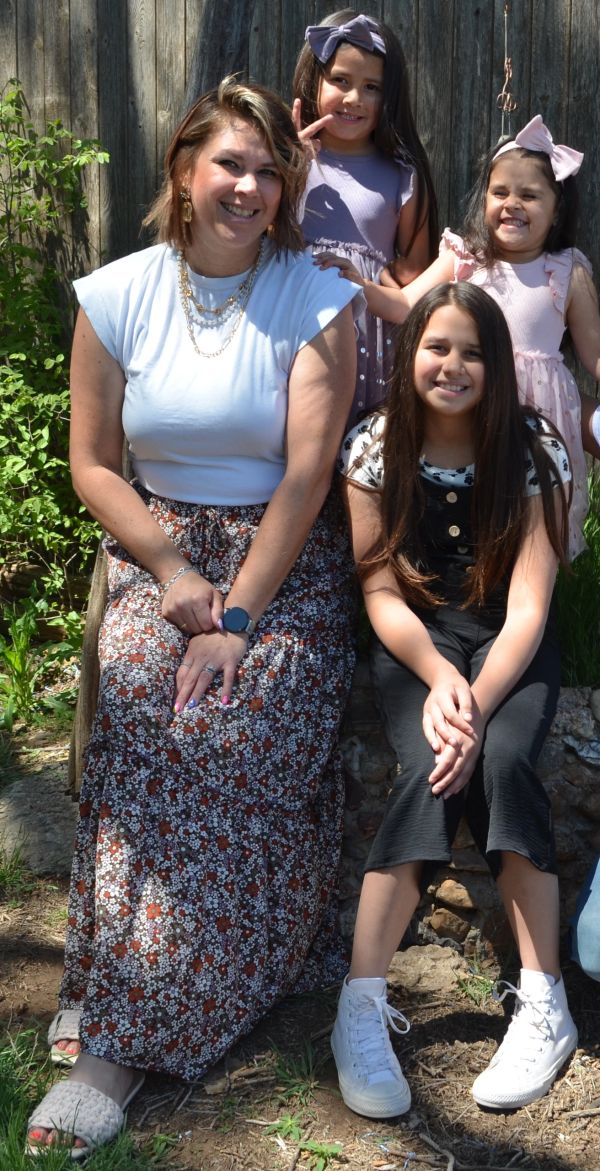 Smiling woman and three girls posing outdoors on a sunny day.