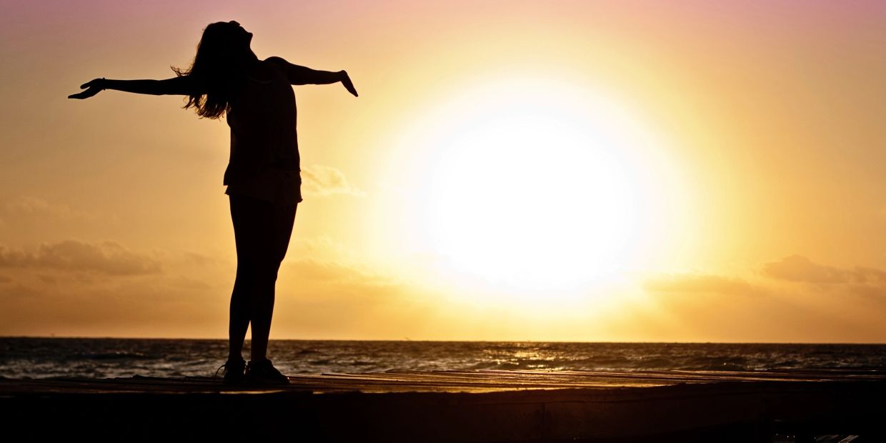 Silhouette of person with arms open at sunset by the sea.