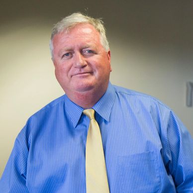 Man in blue shirt and yellow tie posing indoors.