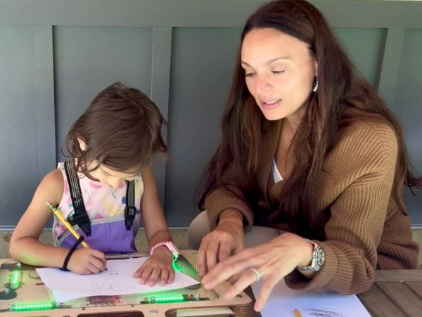 Adult teaching child drawing at a table.