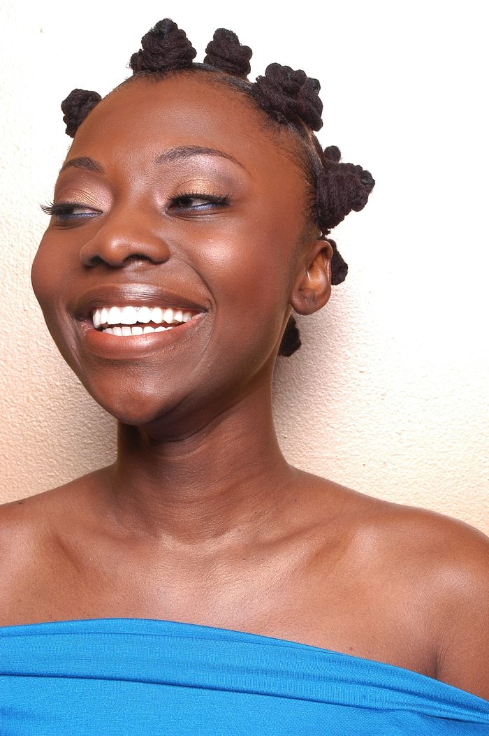 A woman smiling with bantu knots hairstyle and blue top.