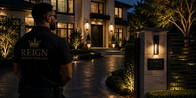 A security guard stands outside a well-lit luxury home at night.