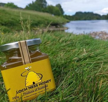 A jar of Loch Ness Honey on grass near a river.