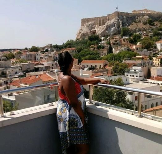 A woman with braided hair enjoys the cityscape and historic Acropolis in the background.