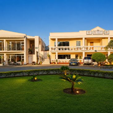 Two beige buildings with cars parked in front and a green lawn.