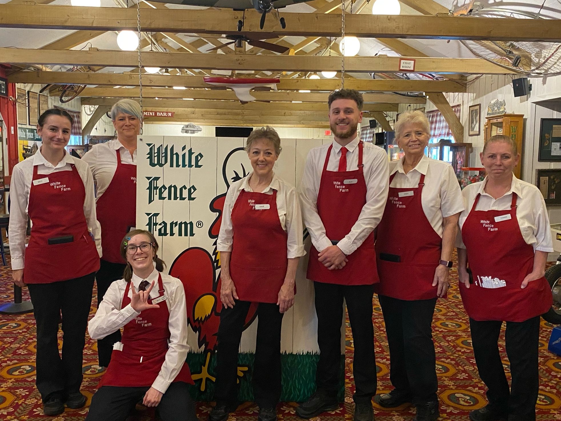 7 employees that are smiling and standing (1 kneeling) in front of a white fence farm sign