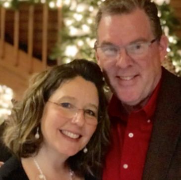 Phil (white male) and Amy (white female) standing together in front of a christmas tree