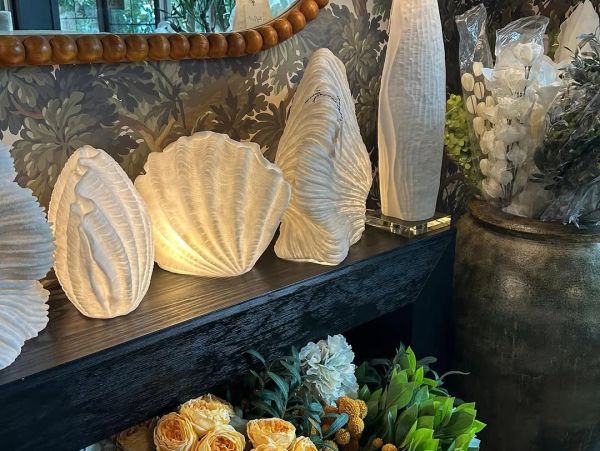 Decorative shell-shaped lamps on a dark wooden shelf with flowers below.