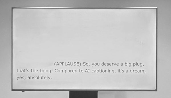 Text on monitor: "You deserve a big plug. Compared to AI captioning, it's a dream, yes, absolutely."