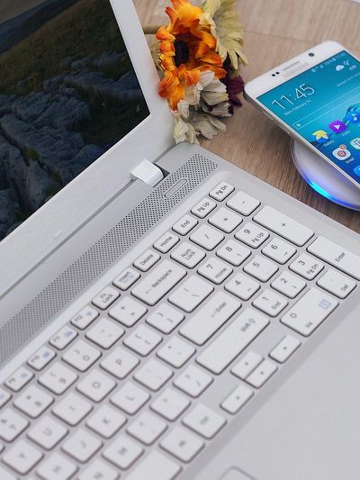 Teclado de laptop branco com um smartphone e flores sobre uma superfície de madeira.