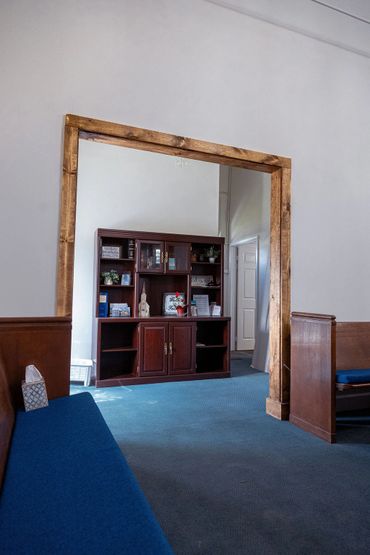 View through wooden frame showing a cabinet and blue cushioned benches in a quiet room.