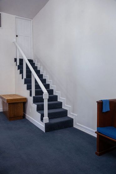 Carpeted stairs leading to a white door in a plain room with blue carpet.