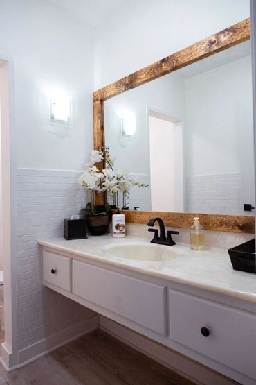 Bright bathroom with wooden-framed mirror and white flowers on the countertop.