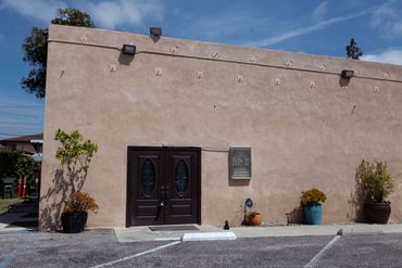 Simple beige building with double dark doors and potted plants.