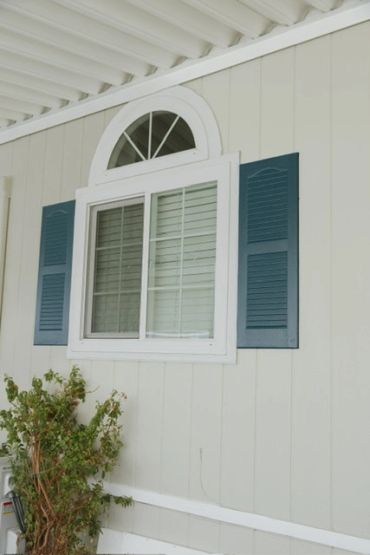 White window with blue shutters on a beige wall.