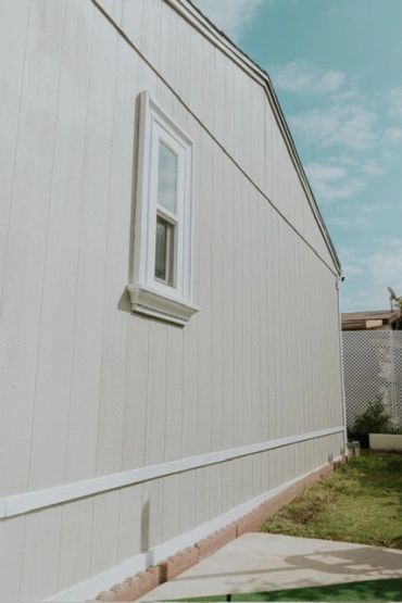 Side view of a light gray house with a small window and green lawn.