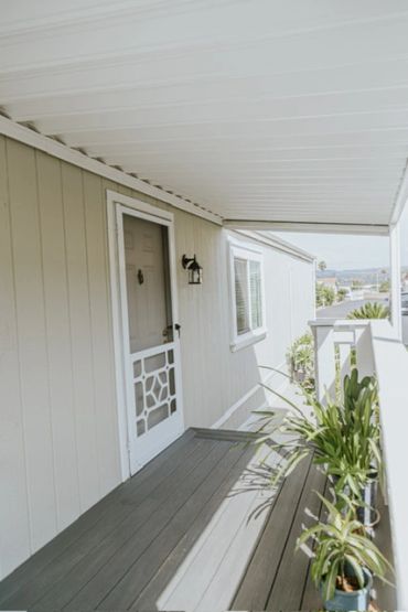 Porch of a beige house with potted plants.