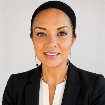 Professional woman with a black headband and blazer smiles confidently.