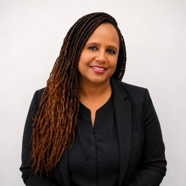 Smiling woman with long braids wearing a black blazer.