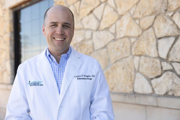 Smiling male doctor in white coat standing outside against stone wall.