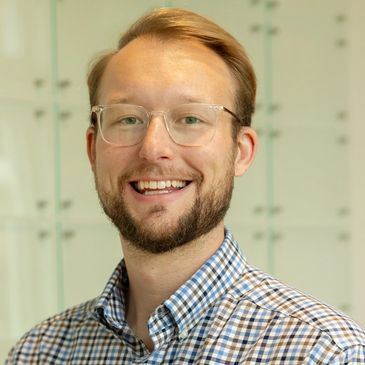 Smiling man with glasses and a checkered shirt.