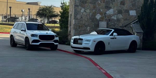 Two luxury white cars parked near a stone building on a sunny day.