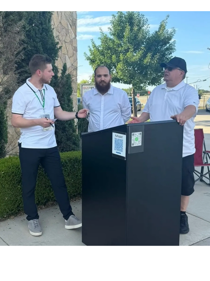 Three men in white shirts standing outdoors by a black podium with QR codes.