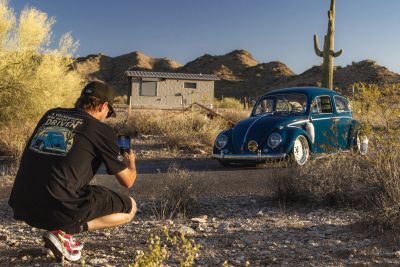 Man photographing a classic blue Volkswagen Beetle in a desert setting.