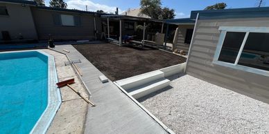 Backyard with a pool, newly laid soil patch, and gravel area beside a house.
