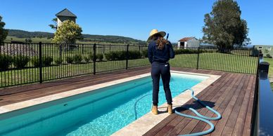 Person cleaning a pool on a sunny day in a rural setting.