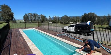 Man working on a small backyard pool under clear blue sky.