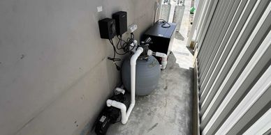 Outdoor pool pump and filtration system setup beside a building wall.