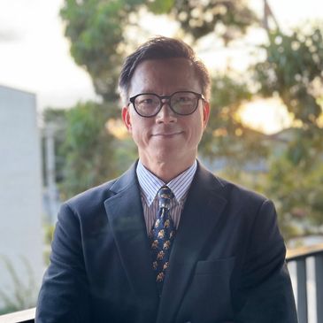 Man in suit and glasses smiling outdoors at sunset.