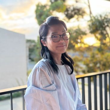 A woman with glasses smiles outdoors during sunset.