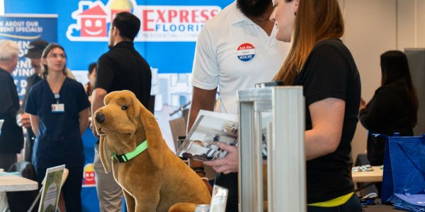 A plush dog toy displayed at a busy trade show booth with attendees interacting.