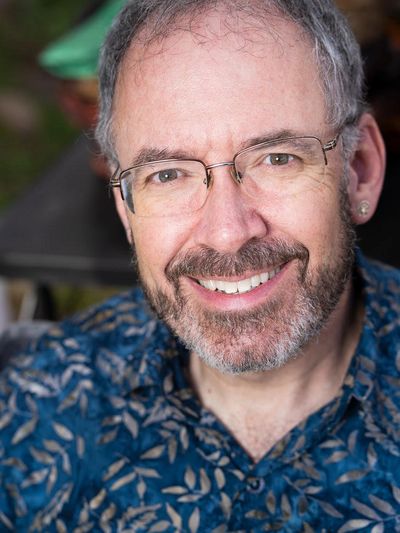 Smiling middle-aged man wearing glasses and a blue patterned shirt.