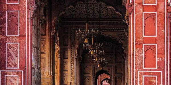 Intricate red and beige archways with chandeliers inside a historic building.