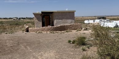 A small, simple building in a dry, open landscape under clear skies.
