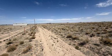 A dirt road runs through a dry, sparsely vegetated landscape under a blue sky.