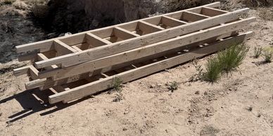 Two wooden ladders lying on sandy ground outdoors.