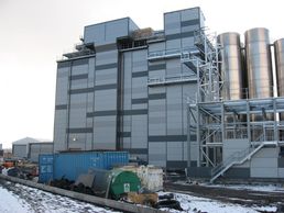 Industrial building with metallic silos and containers in a snowy setting.