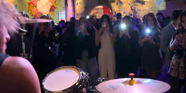 Audience captures a live drum performance in a dimly lit venue.