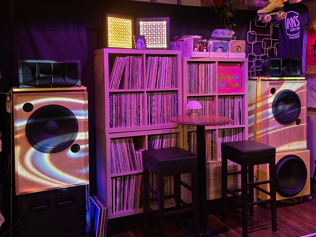 Cozy vinyl bar corner with records, speakers, and a table with stools.