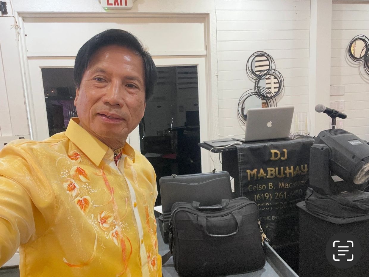 Man in a yellow floral shirt taking a selfie near DJ equipment.