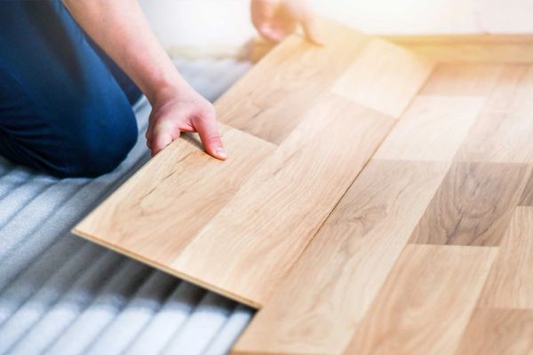 Person installing wooden floor panels.