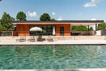 Modern wooden house with pool and lounge chairs.