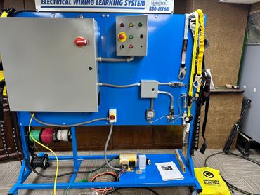 An electrical wiring learning system setup with various components and safety gear.