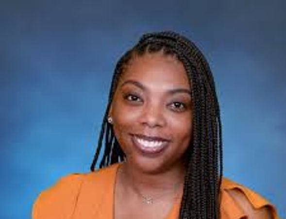 Smiling woman with braided hair wearing an orange top against a blue background.