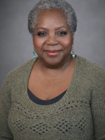 Smiling older woman with short gray hair wearing a green sweater and turquoise earrings.
